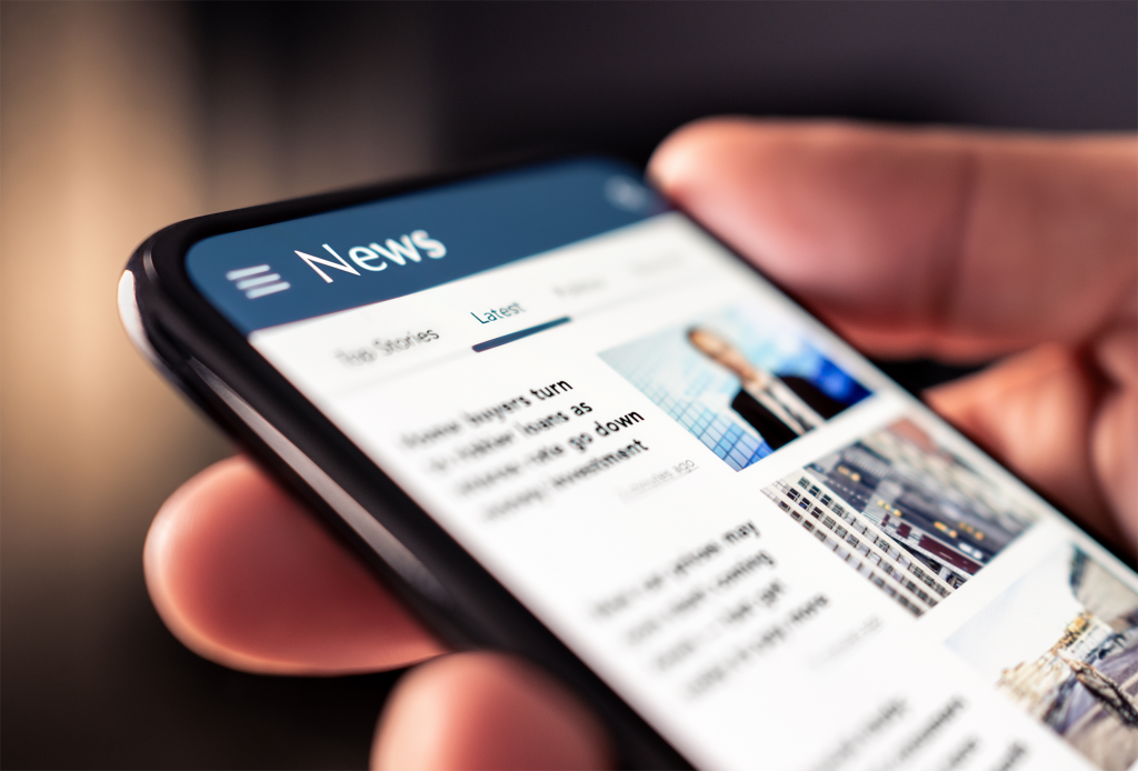 Closeup of hands holding a mobile phone. On the screen is the news- made up of text and images.
