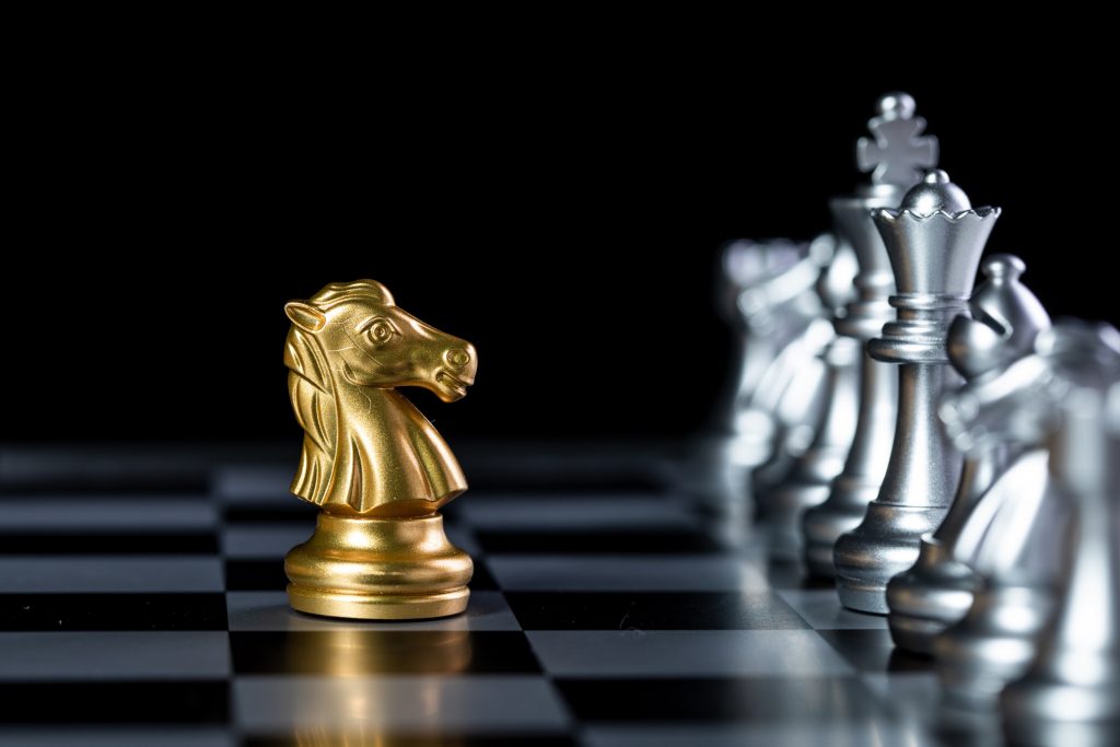 A golden knight chess piece facing a row of silver chess pieces on a black-and-white chessboard, symbolizing bold, strategic thinking and the courage to take unconventional steps in a challenging environment.
This description emphasizes the metaphor of intellectual courage (taking a stand, thinking strategically) and ties well to the idea of learning and adapting to new tools like GenAI in education.