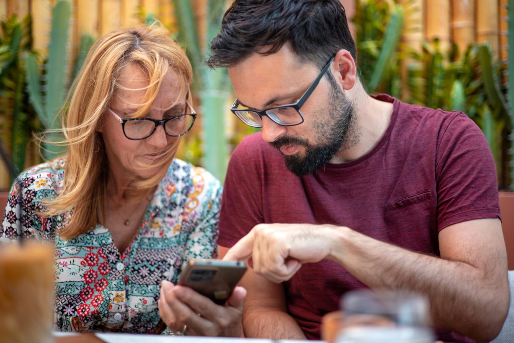 Senior lady and young adult man sharing fun moment on phone — generational gap, technology connection